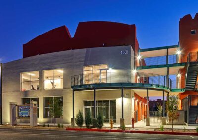 A two-story building with a modern architectural design, featuring large windows, exterior staircases, and a combination of neutral and red colors. The building is numbered 400 and is lit by streetlights in the evening.